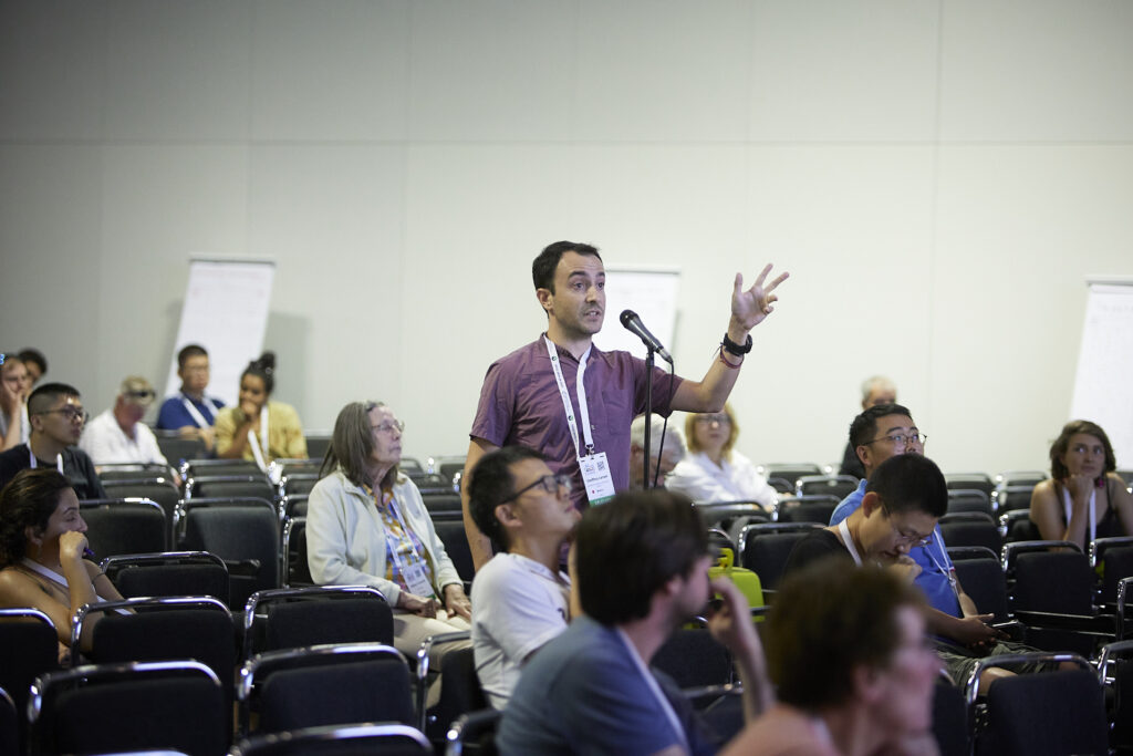 An early career IAVCEI community member asks a question at a microphone at the IUGG23 ECS event.